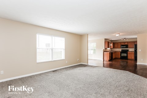 A spacious living room with a grey carpet and a kitchen in the background.