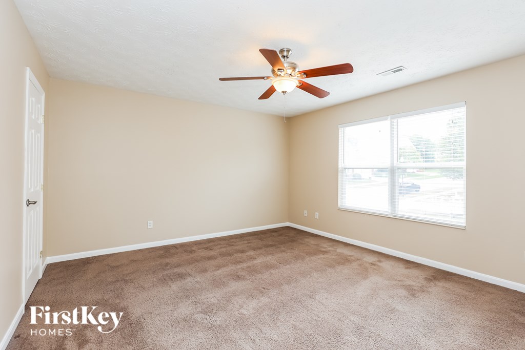 A room with a carpeted floor, a ceiling fan, and a window.