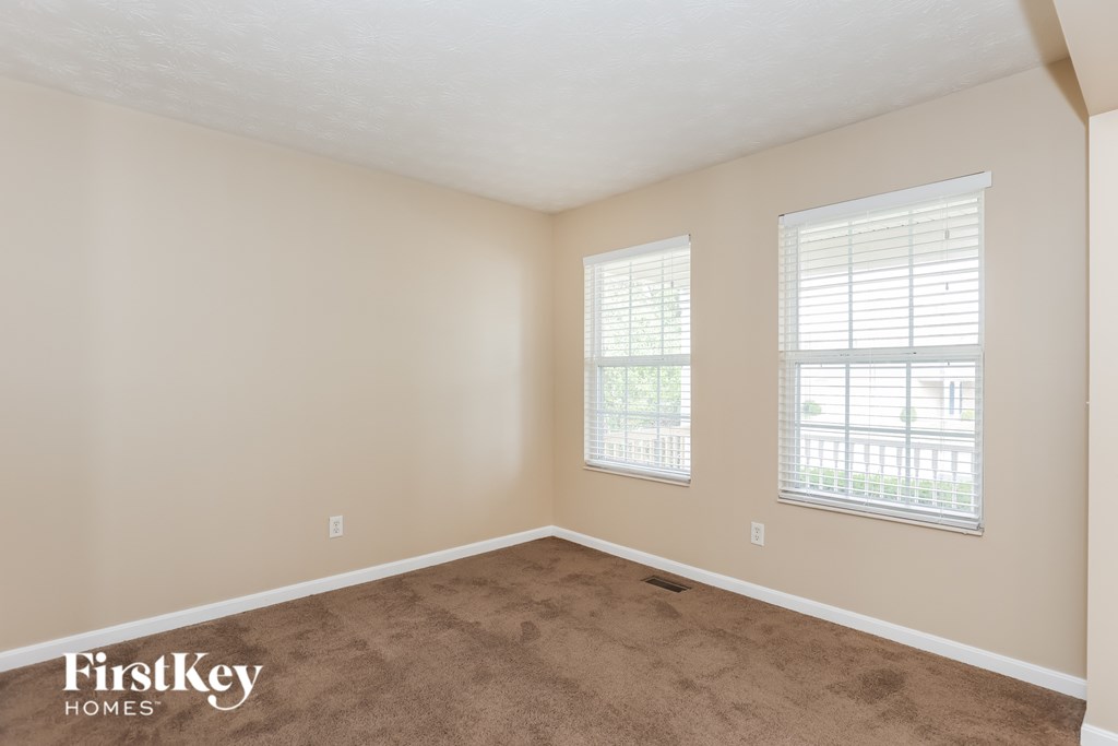 A room with a carpeted floor and two windows.