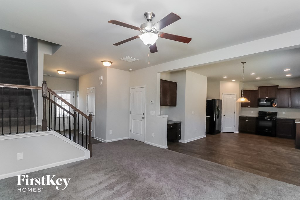 A spacious living room with a ceiling fan and a staircase.