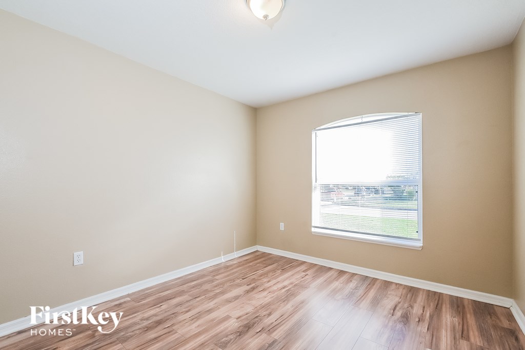 A room with wooden flooring and a window showing a view of a grassy area outside.