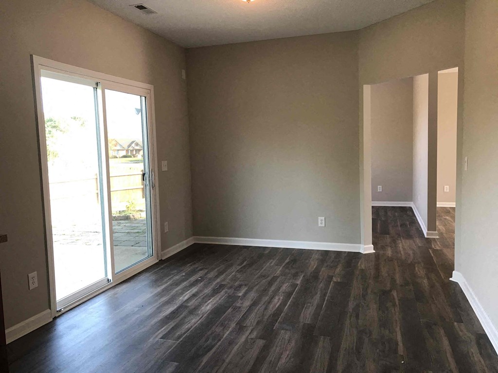 A room with a sliding glass door and wood flooring.