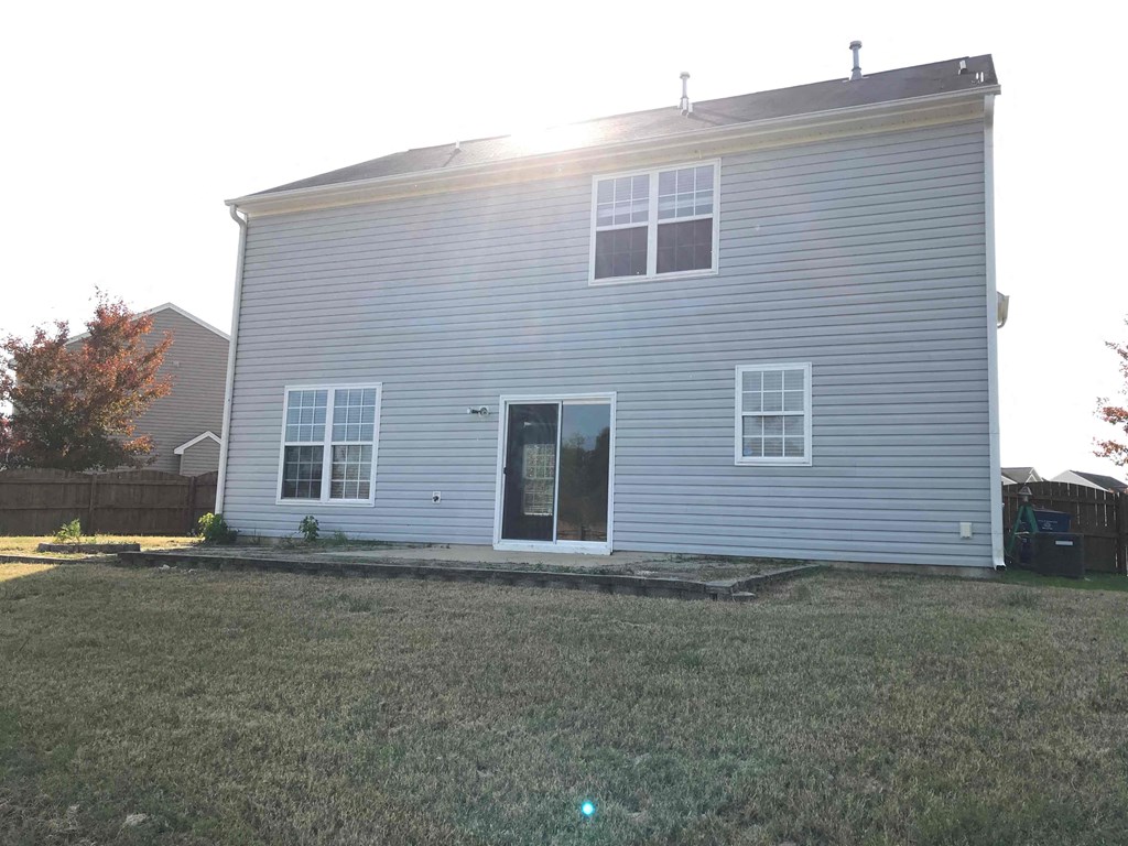 A house with a grey siding and a black door is surrounded by a grassy area.