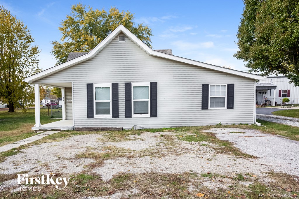 a small white house with black shutters and a gravel driveway