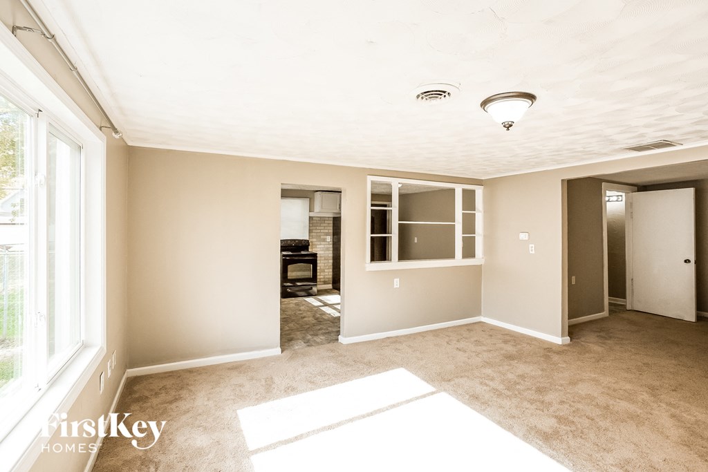 an empty living room with a large window and a door to a kitchen