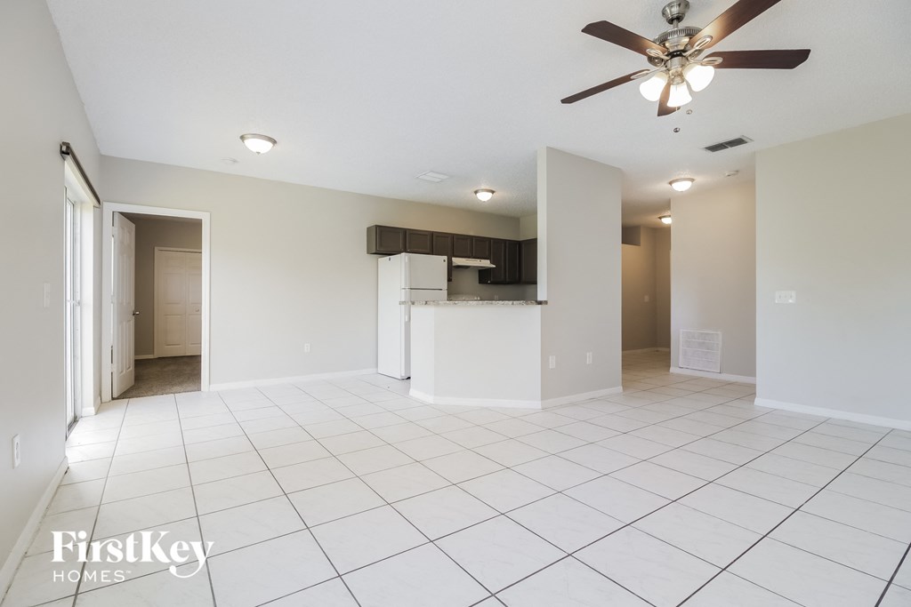an empty living room with a ceiling fan and a kitchen