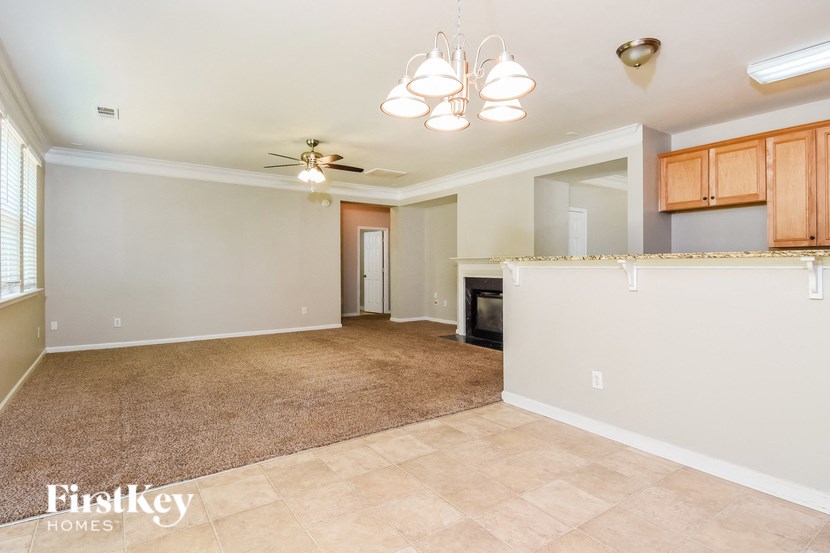 an empty living room with a kitchen and a ceiling fan