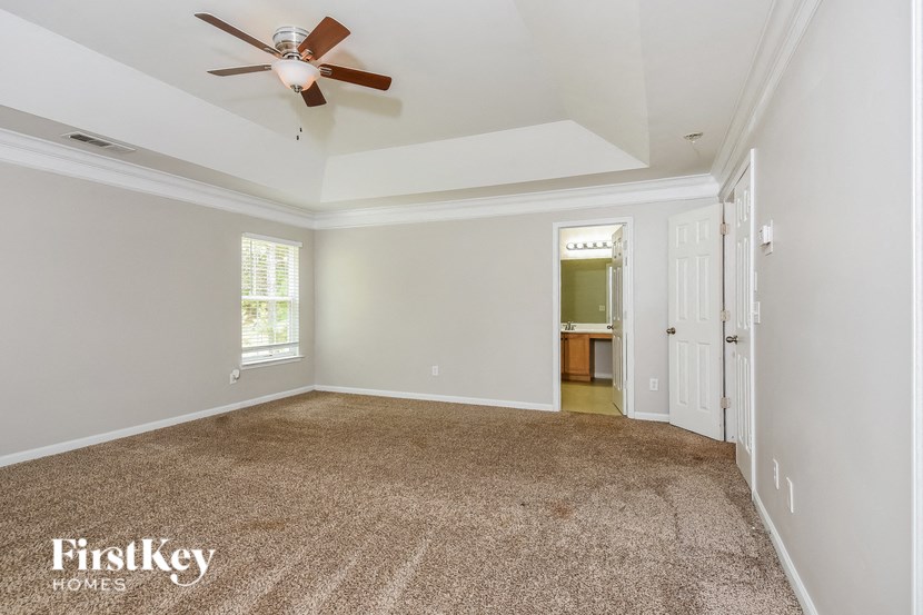 an empty living room with a ceiling fan and a door to a bathroom