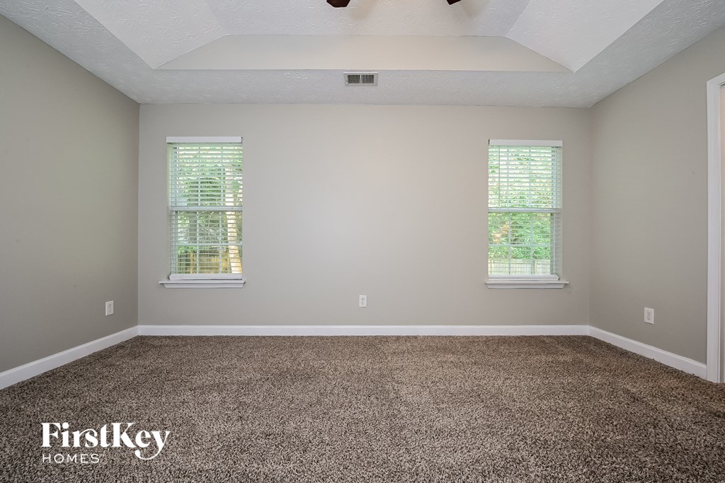 A room with a carpeted floor and two windows.