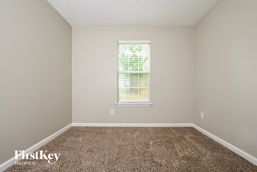 A room with a carpeted floor and a window with blinds.