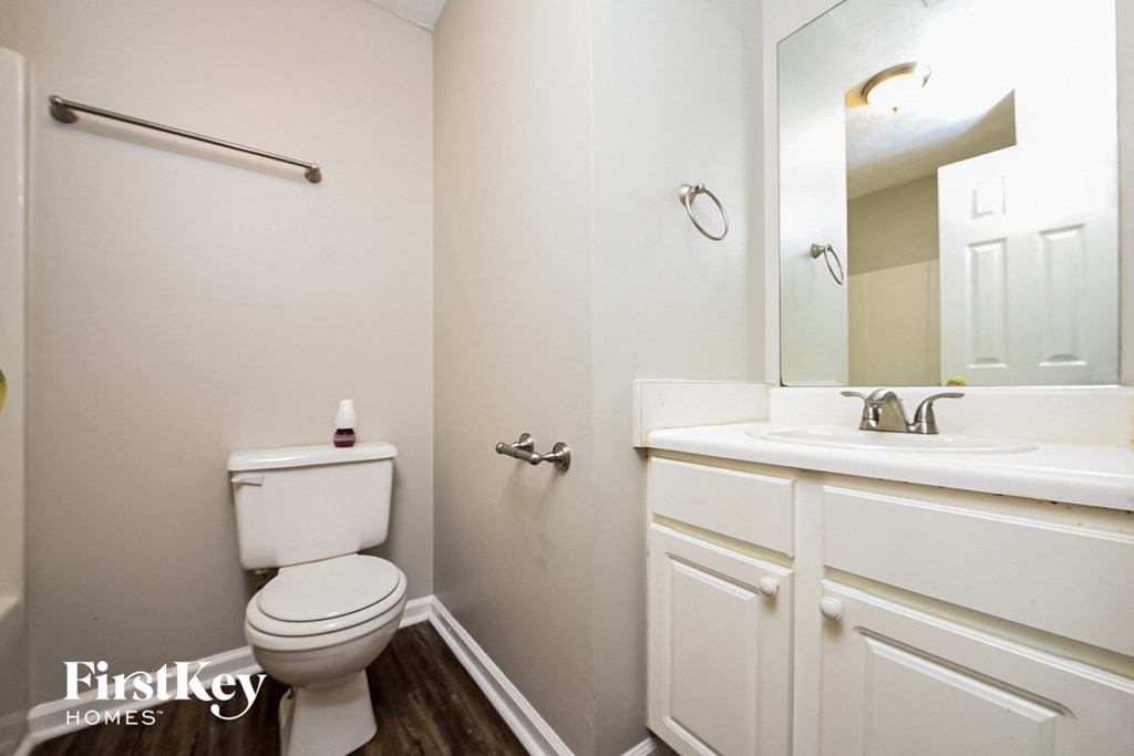 A white toilet sits in a small bathroom with a white sink and a mirror.