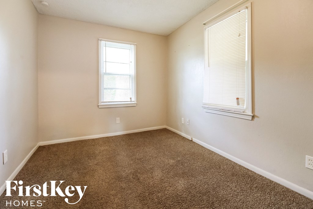 an empty room with carpet and two windows