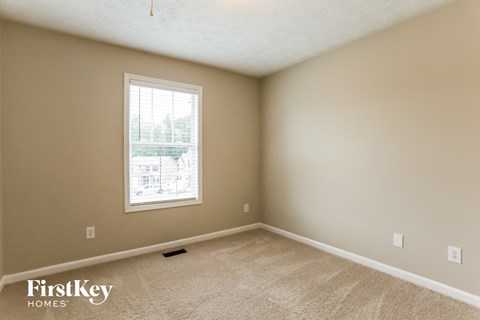 A room with a carpet floor and a window showing a view of a building outside.