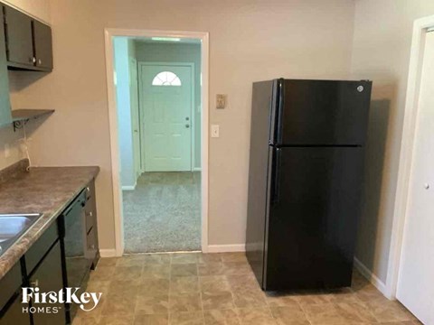 A black refrigerator in a kitchen with a sink and cabinets.