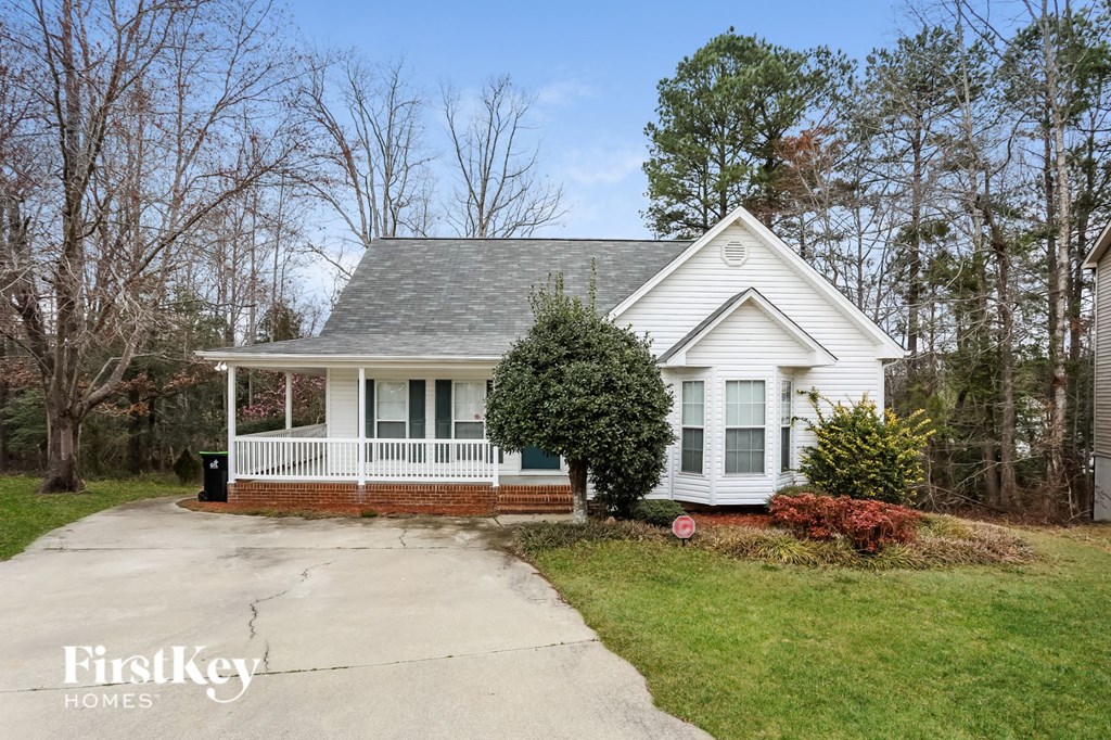 A white house with a porch and a tree in front.