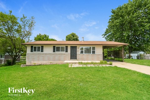 A house with a brown roof and a white wall is surrounded by a green lawn.