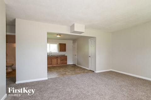 A carpeted room with a kitchen in the background.