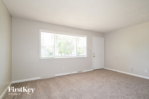 A room with a carpeted floor and a window with a view of trees.