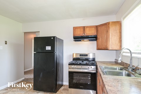 A black refrigerator is in a kitchen with wooden cabinets and stainless steel appliances.
