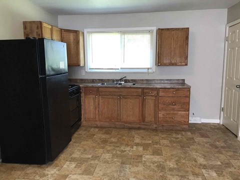 A kitchen with a black fridge, wooden cabinets, and a checkered floor.