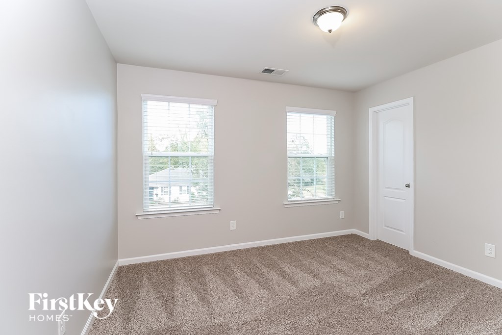 A room with a carpeted floor and two windows.