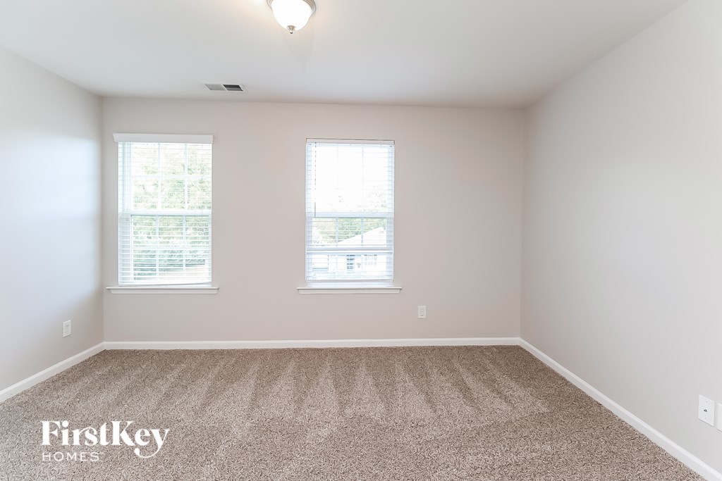 A room with a carpeted floor and two windows.