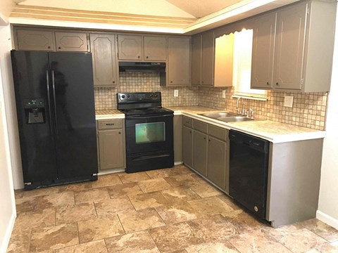 A kitchen with black appliances and brown tiled flooring.