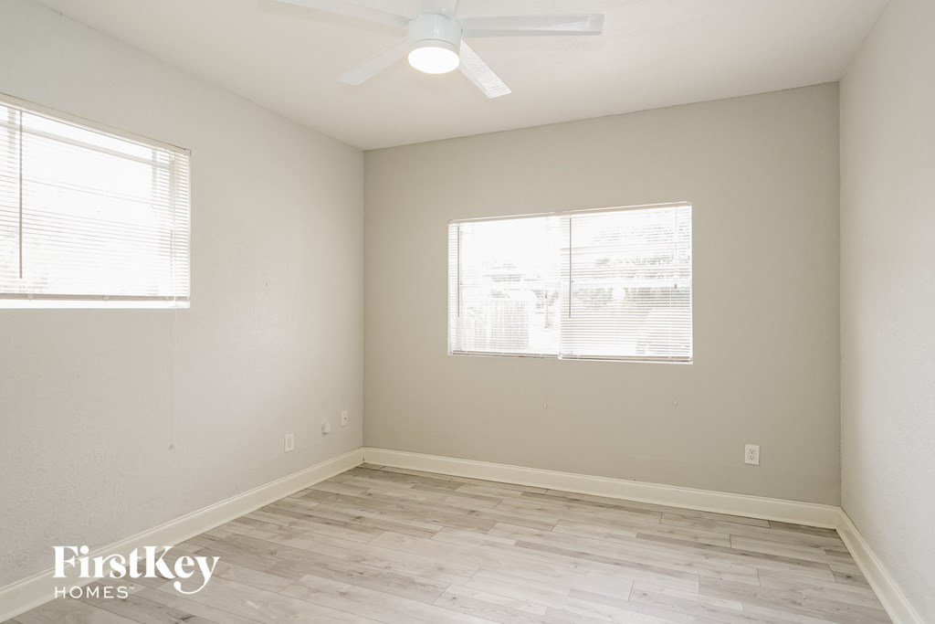 a bedroom with wood floors and white walls and two windows