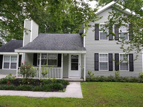 A house with a grey siding and a white door is surrounded by greenery.