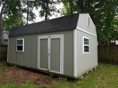 A small grey shed with a black roof and a white door.