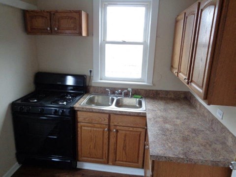 A black stove in a kitchen with wooden cabinets and a window.