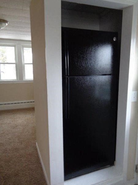 A black fridge in a room with a carpeted floor.