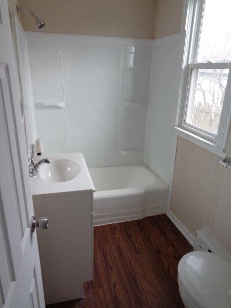 A white bathroom with wood floors and a window.