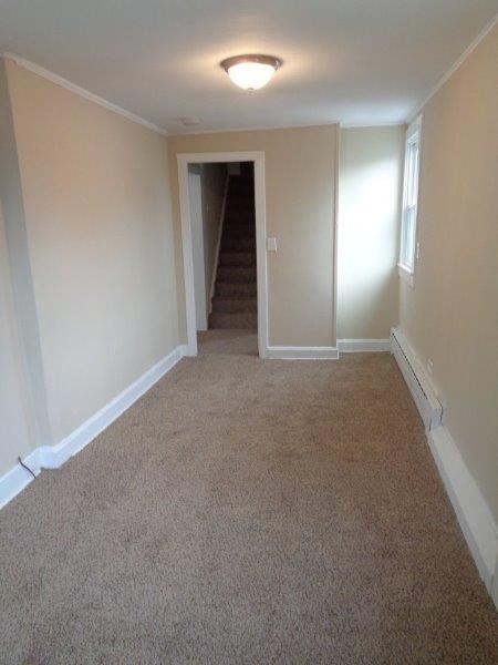 A hallway with a carpeted floor and a staircase leading to another room.