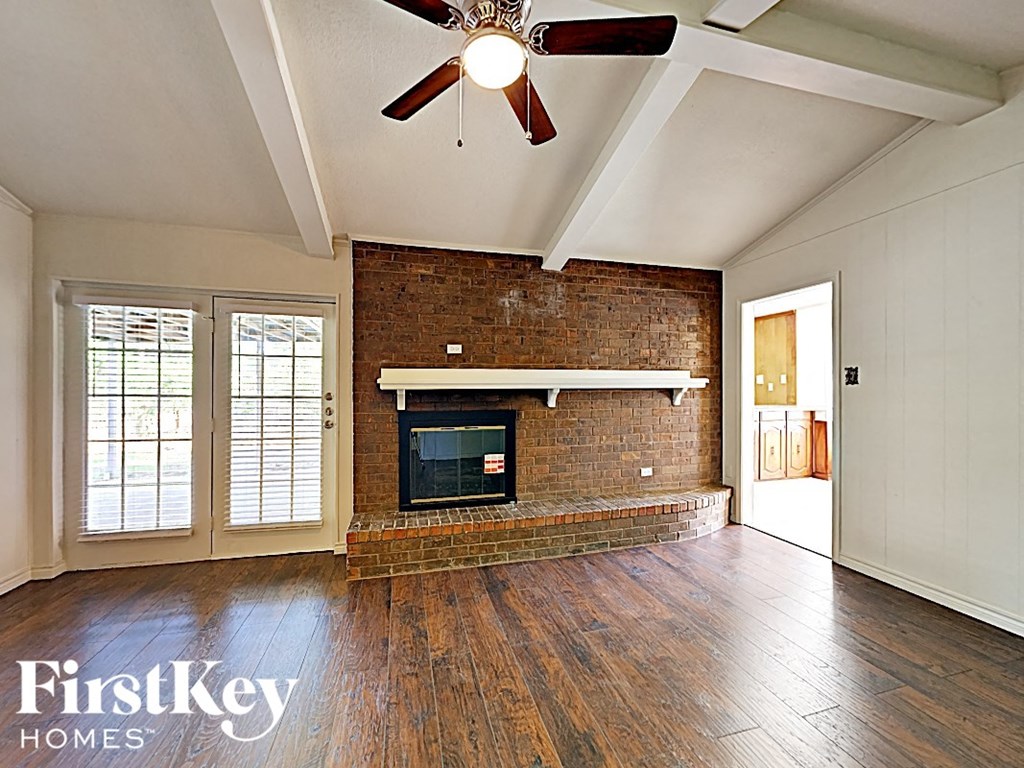 A room with a brick fireplace and wood floors.