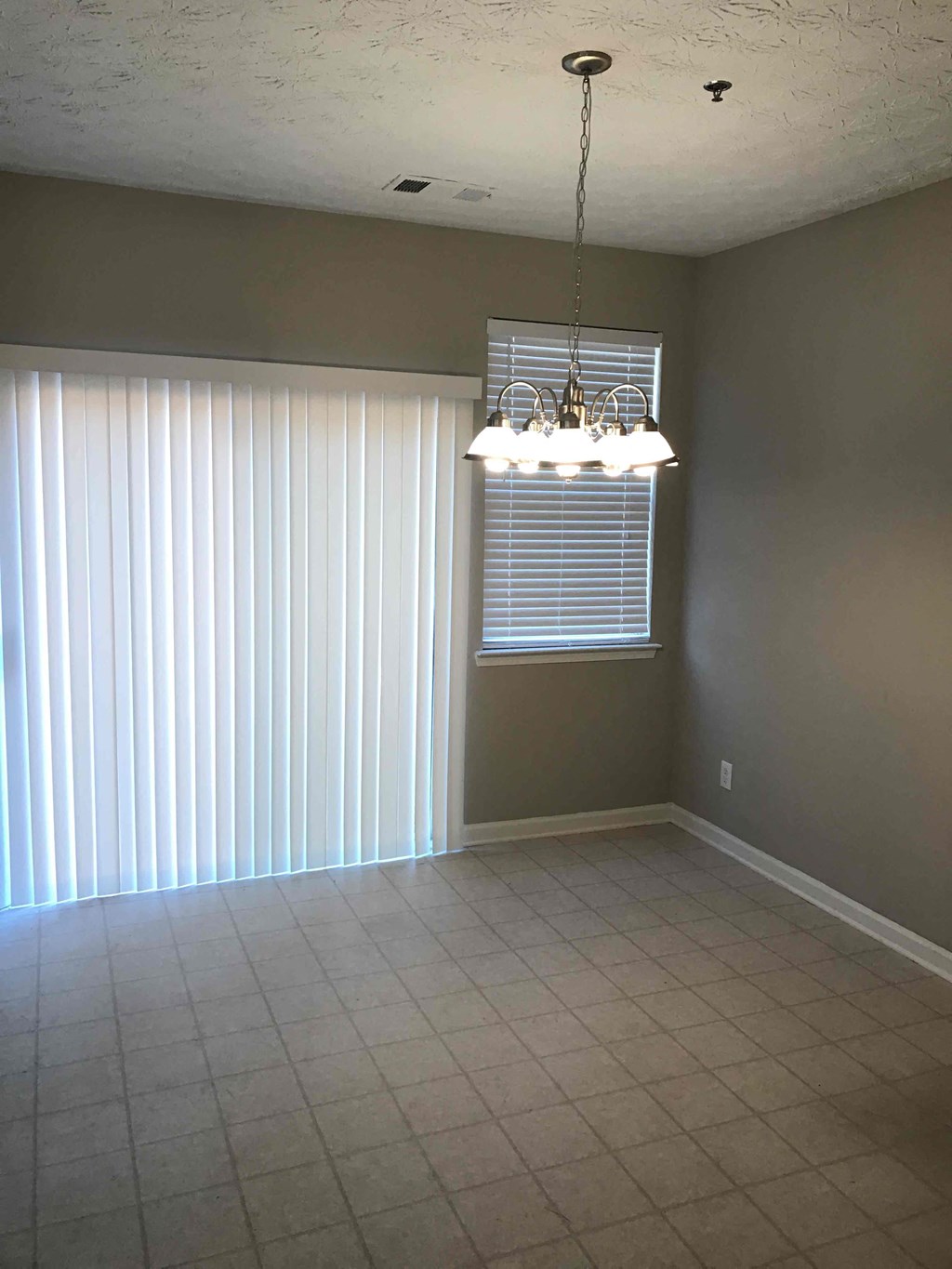 an empty living room with window blinds and a chandelier