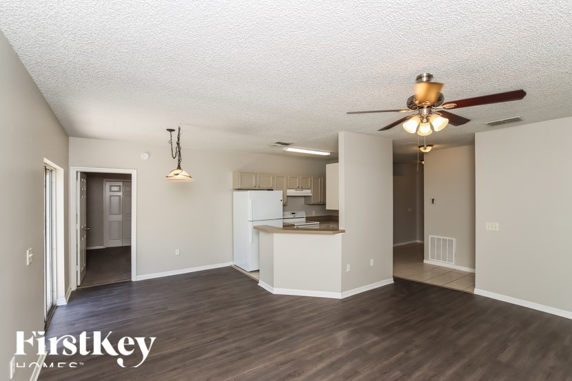 A spacious living room with a kitchen in the background and a ceiling fan above.