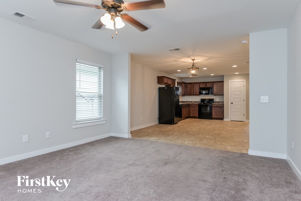 an empty living room with a ceiling fan and a kitchen