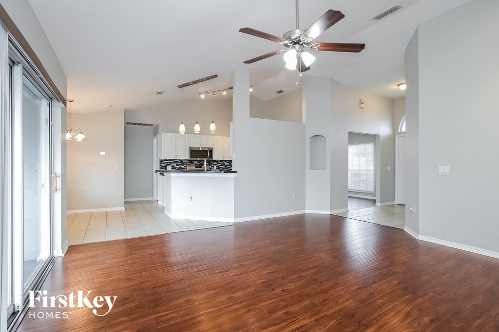 A spacious living room with a wooden floor and a ceiling fan.