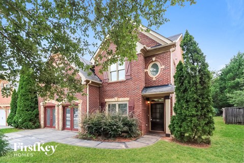 the front of a brick house with a yard and trees