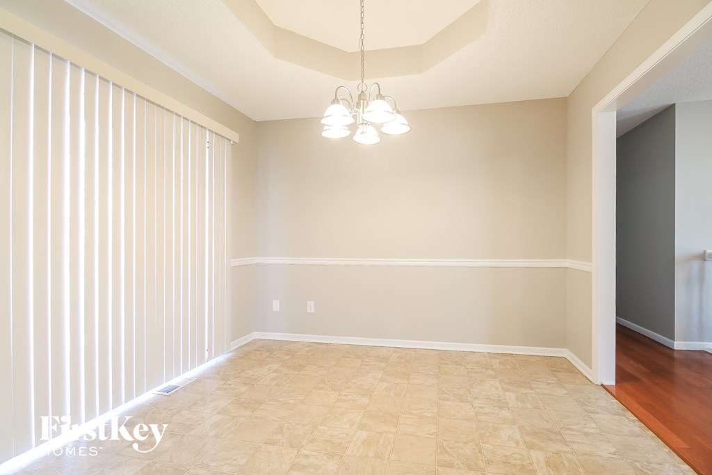 an empty dining room with white blinds and a chandelier
