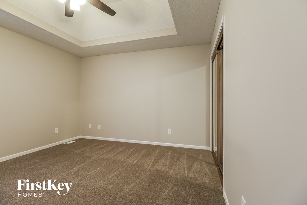 the spacious living room with carpeted flooring and a ceiling fan