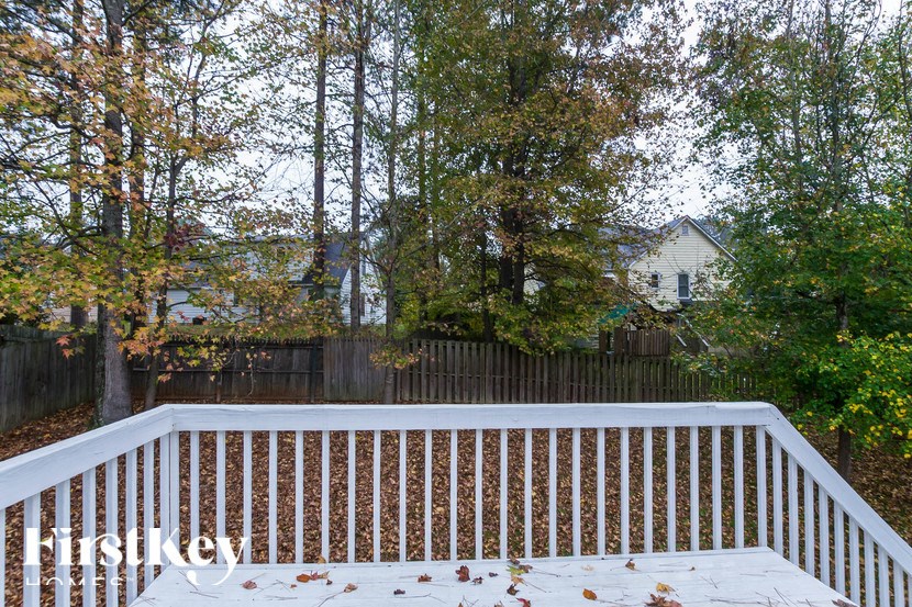 a deck with a fence and trees and a house in the background