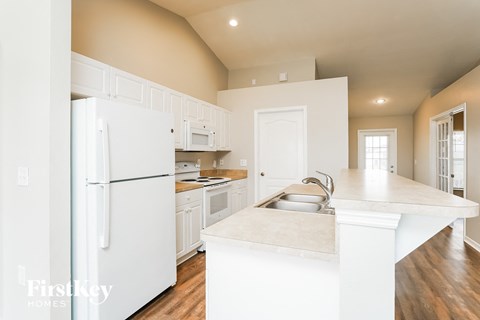 A white kitchen with a refrigerator, sink, and cabinets.