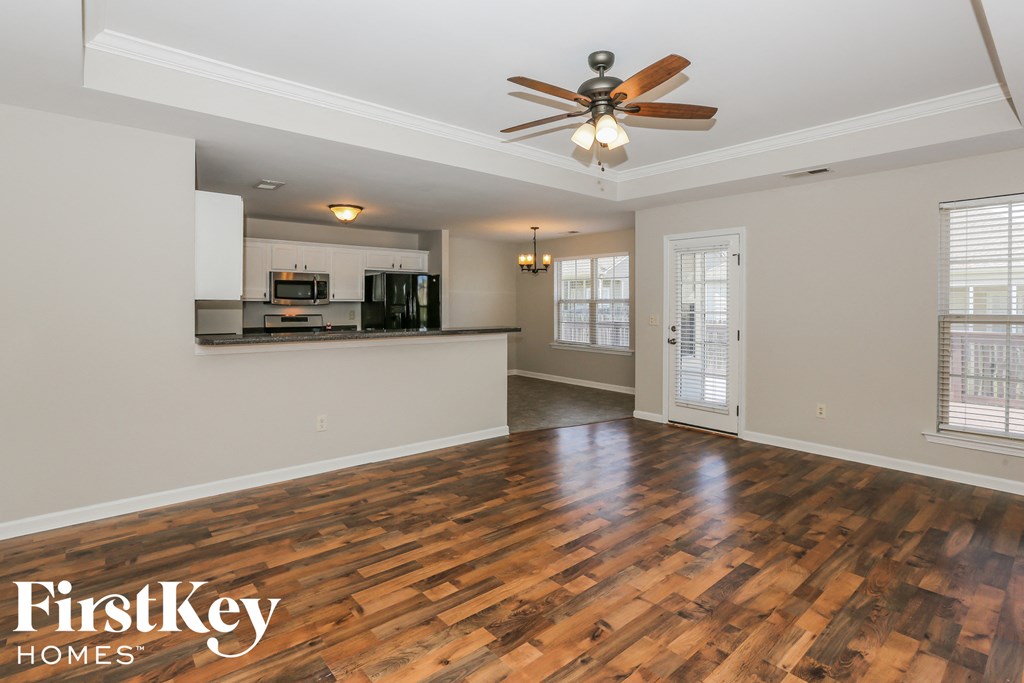 an empty living room with a ceiling fan and a kitchen