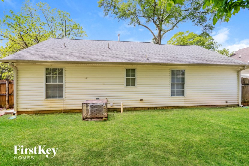 the back of a white house with a grill in the grass