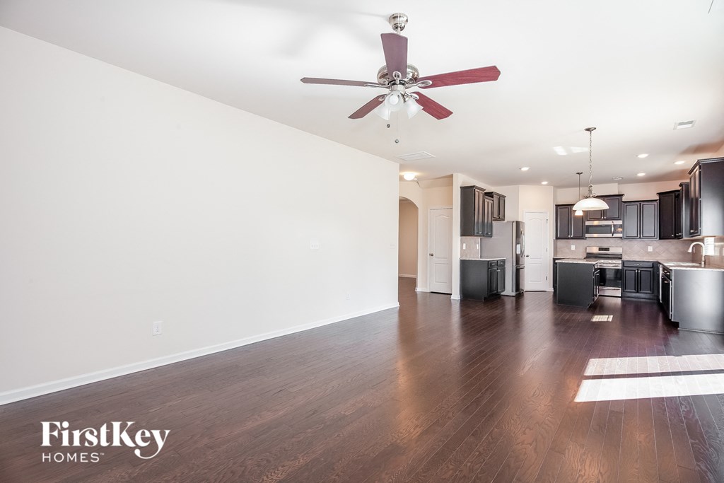 an empty living room with a ceiling fan and a kitchen