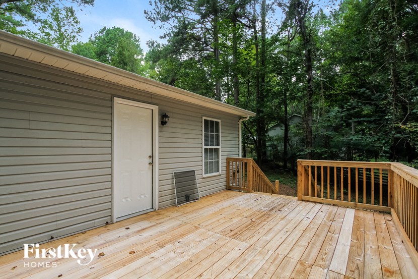A wooden deck with a white door and a window is surrounded by trees.