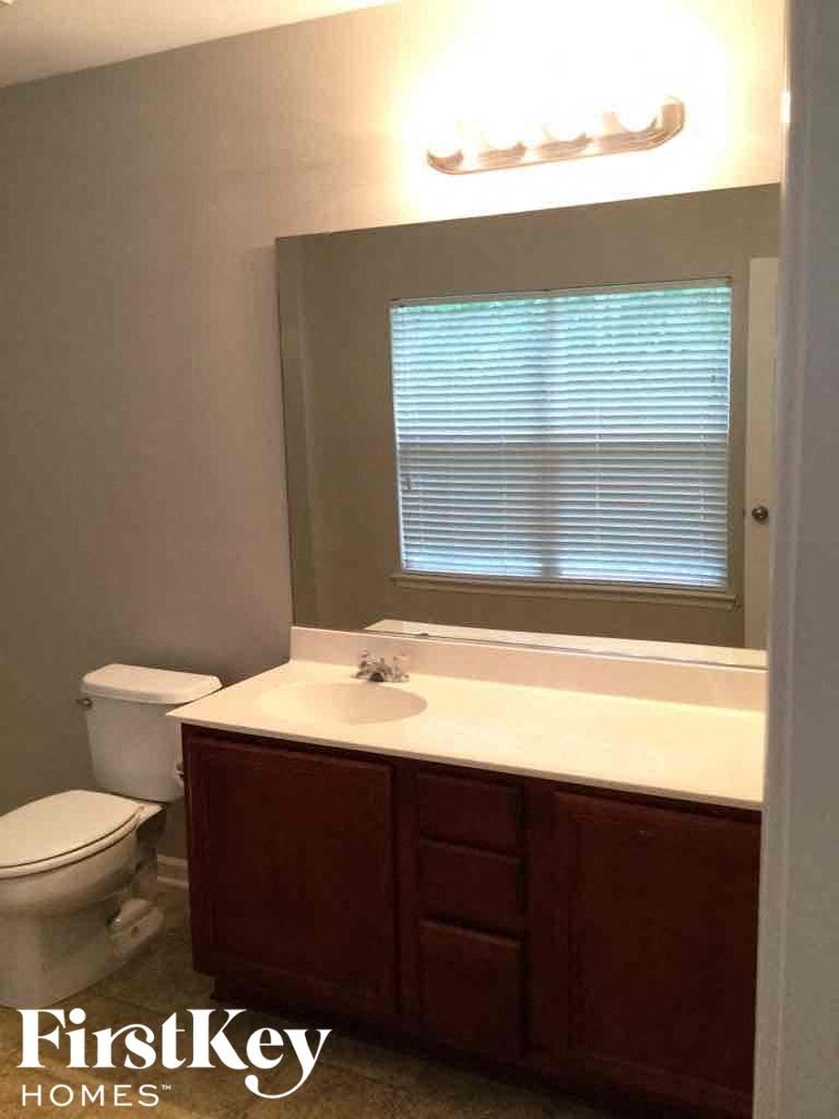 A bathroom with a toilet, sink and a window with blinds.