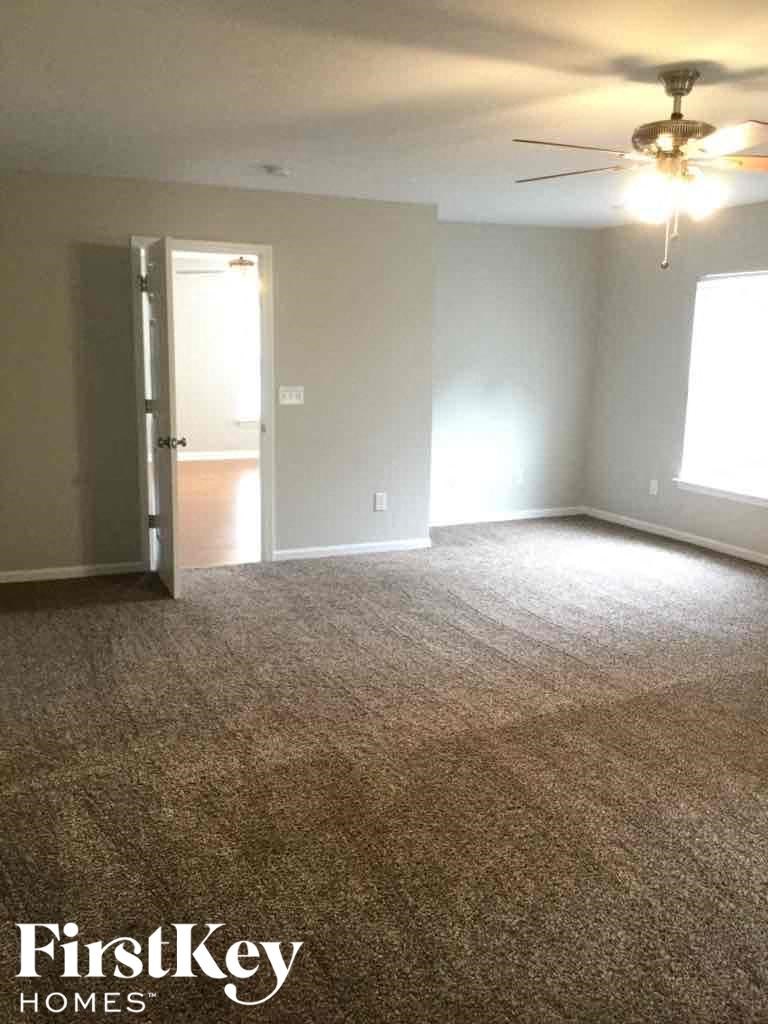 A carpeted room with a ceiling fan and a doorway leading to another room.